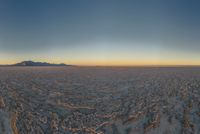 a wide picture of a snowy plain surrounded by mountains and desert land at sunrise time