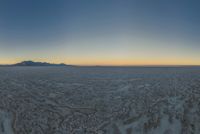 a wide picture of a snowy plain surrounded by mountains and desert land at sunrise time