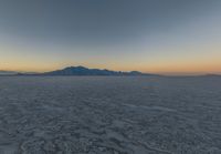 a wide picture of a snowy plain surrounded by mountains and desert land at sunrise time