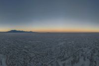 a wide picture of a snowy plain surrounded by mountains and desert land at sunrise time