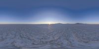 a wide panoramic view of snow and mountain range in the background with the sun setting