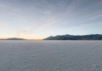 the sky is getting darker as the sun begins to set over the snowy landscape, mountains and distant land