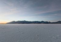 the sky is getting darker as the sun begins to set over the snowy landscape, mountains and distant land