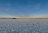 a person with a snowboard on an icy surface at sunset behind a tower, in the distance is a large body of water