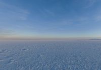 a person with a snowboard on an icy surface at sunset behind a tower, in the distance is a large body of water