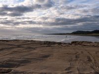 the sun is shining through dark clouds above a beach and ocean near a rocky shoreline