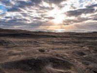 the sun is shining through dark clouds above a beach and ocean near a rocky shoreline