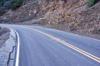 a single highway going up a rocky hill slope near some trees and rocks on one side