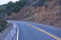 a single highway going up a rocky hill slope near some trees and rocks on one side