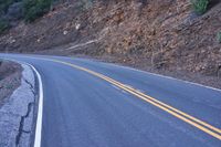 a single highway going up a rocky hill slope near some trees and rocks on one side