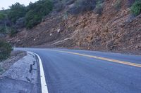 a single highway going up a rocky hill slope near some trees and rocks on one side