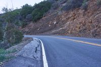 a single highway going up a rocky hill slope near some trees and rocks on one side