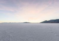 two skiers ride across the open frozen lake at sunset while a fog covers the mountains in the distance