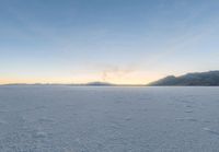 two skiers ride across the open frozen lake at sunset while a fog covers the mountains in the distance