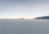 two skiers ride across the open frozen lake at sunset while a fog covers the mountains in the distance