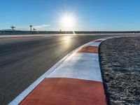 a photo of a dirt race track with sun setting in the distance of the track