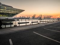 the sunset sets behind the waterfront where the city is setting at dusk, with cars parked along the shoreline and large glass windows on top of the building