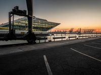 the sunset sets behind the waterfront where the city is setting at dusk, with cars parked along the shoreline and large glass windows on top of the building