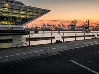 the sunset sets behind the waterfront where the city is setting at dusk, with cars parked along the shoreline and large glass windows on top of the building