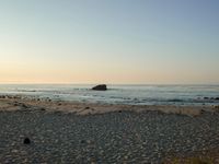 there is a lone surf board on the beach near the water and rock stacks in the distance