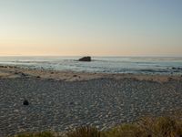 there is a lone surf board on the beach near the water and rock stacks in the distance