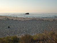 there is a lone surf board on the beach near the water and rock stacks in the distance