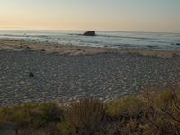 there is a lone surf board on the beach near the water and rock stacks in the distance