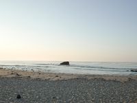 there is a lone surf board on the beach near the water and rock stacks in the distance