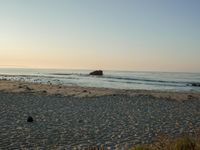 there is a lone surf board on the beach near the water and rock stacks in the distance