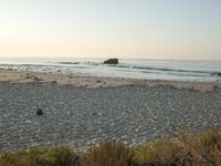 there is a lone surf board on the beach near the water and rock stacks in the distance