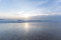 a small surfboard is on the water on a sandy beach at sunrise time, with clouds in the sky