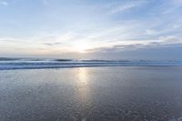 a small surfboard is on the water on a sandy beach at sunrise time, with clouds in the sky