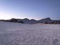 a sandy hill covered in desert rocks and snow on the mountain side with a clear sky overhead