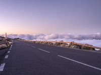 an empty winding road on a mountain with the sun set above the mountains in the background