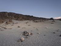 a sandy ground with rocks in the background at dusk time near a mountain range or desert