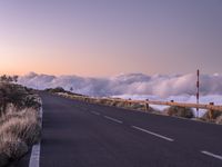 an empty winding road on a mountain with the sun set above the mountains in the background