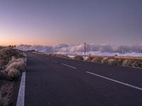 an empty winding road on a mountain with the sun set above the mountains in the background