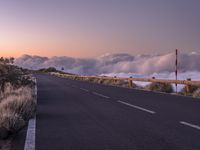 an empty winding road on a mountain with the sun set above the mountains in the background