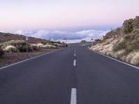 an empty winding road on a mountain with the sun set above the mountains in the background