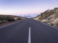 an empty winding road on a mountain with the sun set above the mountains in the background