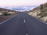 an empty winding road on a mountain with the sun set above the mountains in the background