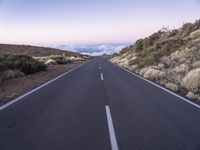 an empty winding road on a mountain with the sun set above the mountains in the background