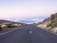 an empty winding road on a mountain with the sun set above the mountains in the background