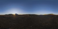 the sun sets over an arid landscape with mountain peaks in the distance and sunlight peeking down