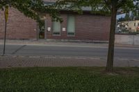 a lone parking meter near a brick building on the street with grass and trees in front