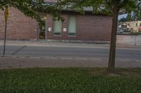 a lone parking meter near a brick building on the street with grass and trees in front