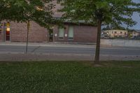 a lone parking meter near a brick building on the street with grass and trees in front