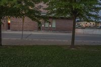 a lone parking meter near a brick building on the street with grass and trees in front