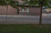 a lone parking meter near a brick building on the street with grass and trees in front