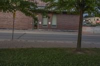 a lone parking meter near a brick building on the street with grass and trees in front